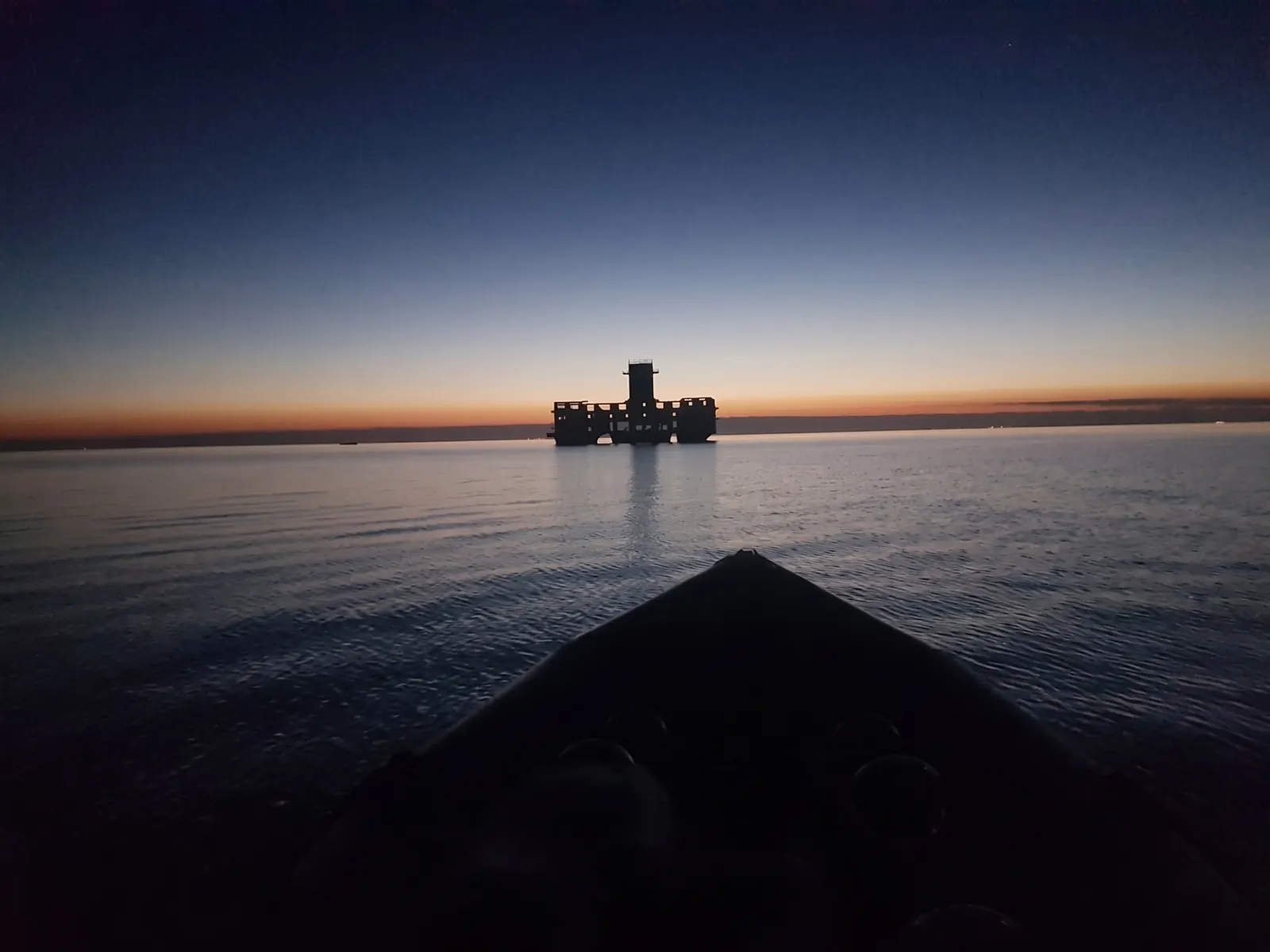 Sylwetka torpedowni na horyzoncie o świcie, na pierwszym planie dziób łodzi