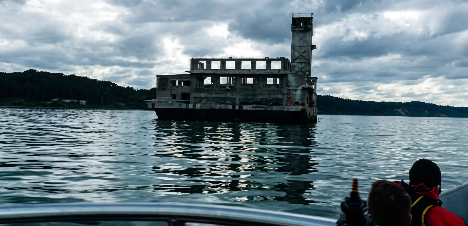 Ruina torpedowni widziana z pokładu motorówki, na rufie pasażerowie w kurtkach